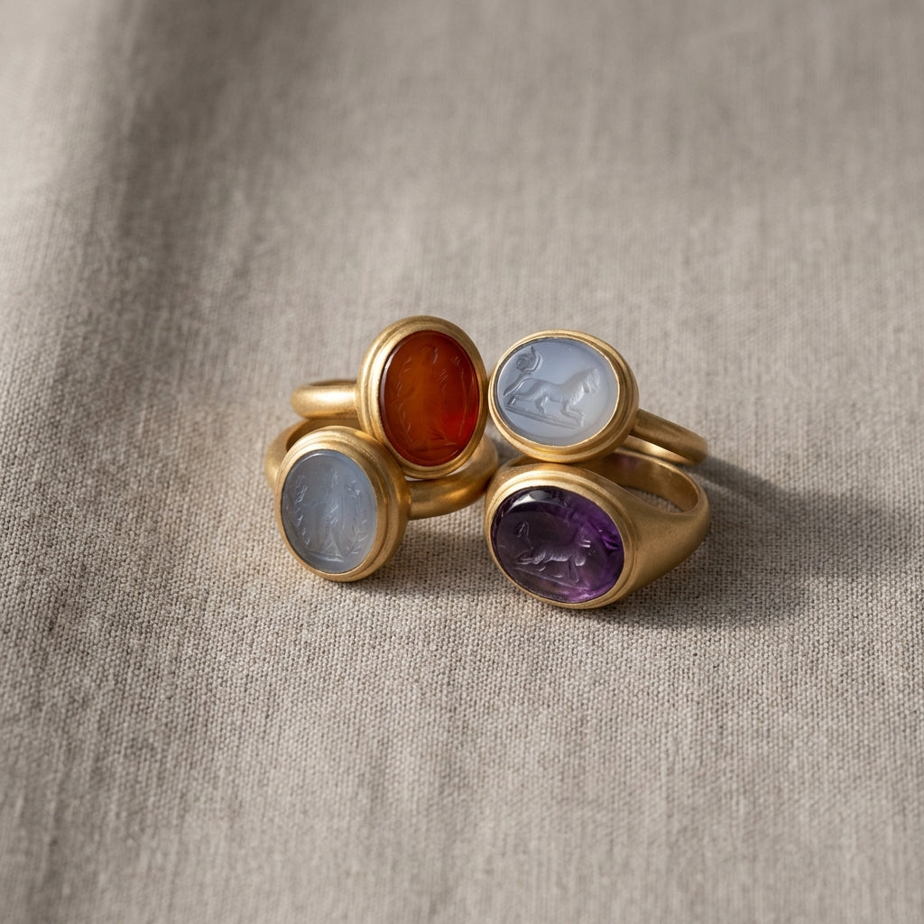 Close overhead photo of a small group of ancient intaglio roman talisman ring pieces on neutral linen background in soft natural light minimalist Aurora Antiqua palette