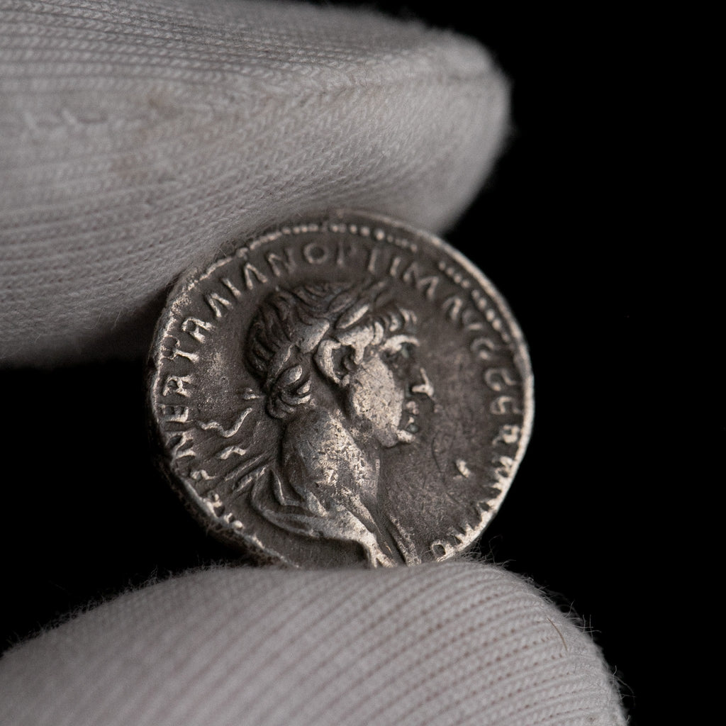 Roman silver denarius of Trajan held for size reference.