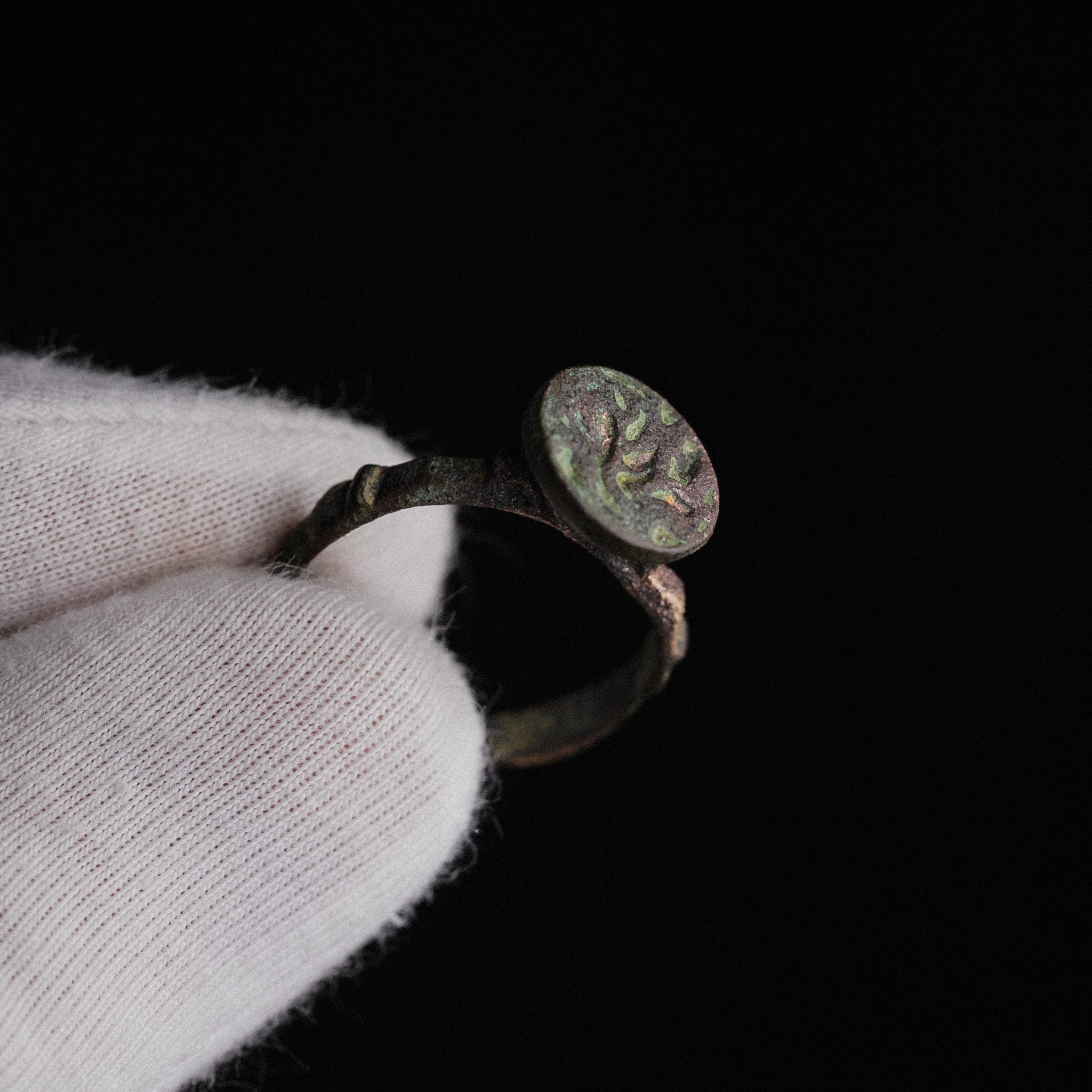 Medieval Islamic bronze signet ring Zahir held in gloved hand, circular bezel with incised Arabic-style script