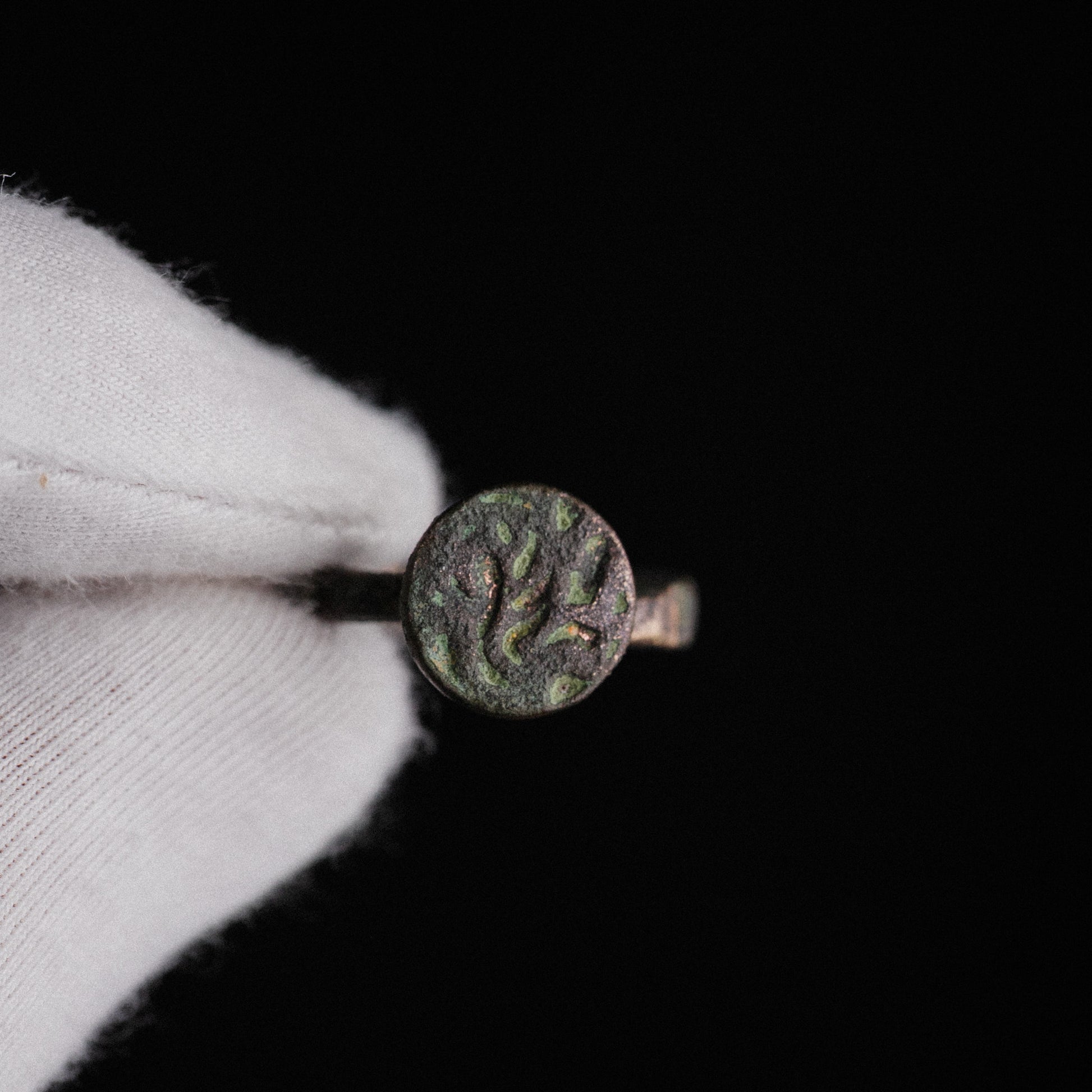 Top view of Zahir medieval Islamic bronze ring bezel with sinuous calligraphic incisions and malachite patina