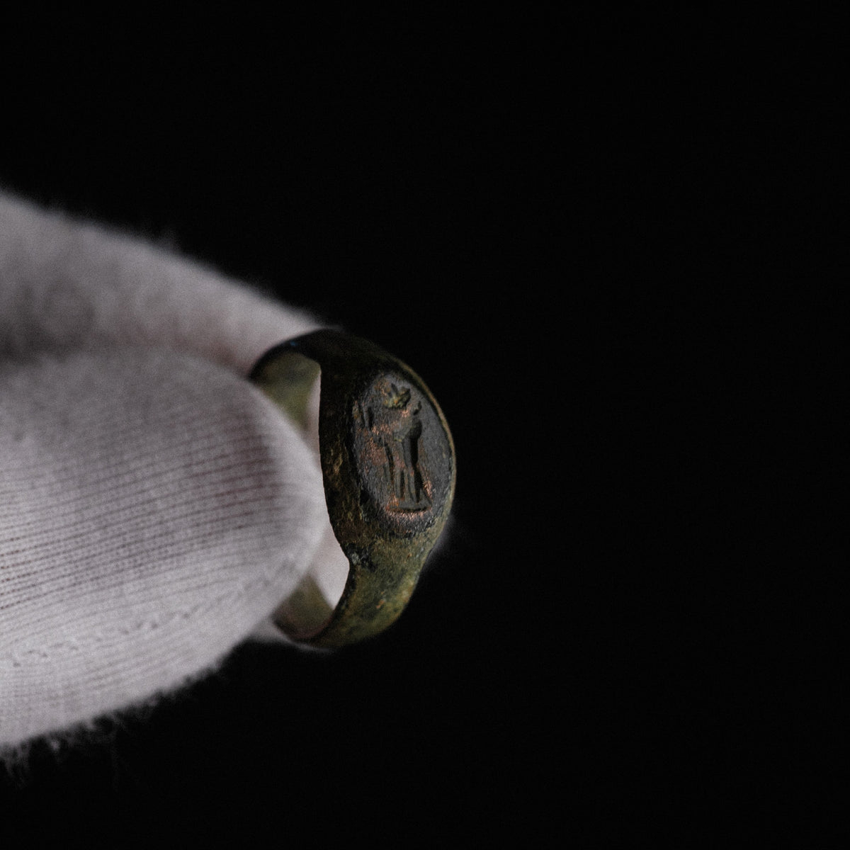 Roman bronze signet ring Numerius Faber held in gloved hand, deity intaglio visible on oval bezel