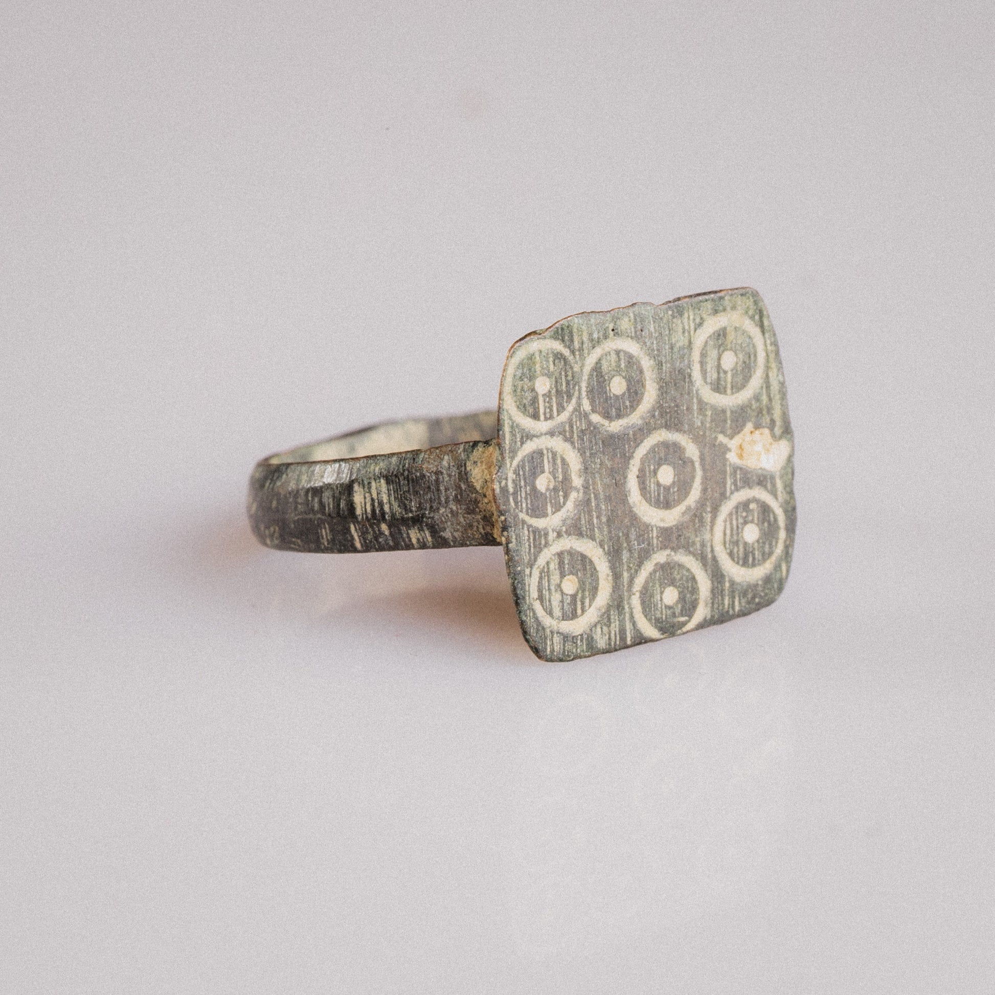 Three-quarter view of Novenarius Roman bronze ring revealing bezel geometry and patina contrast
